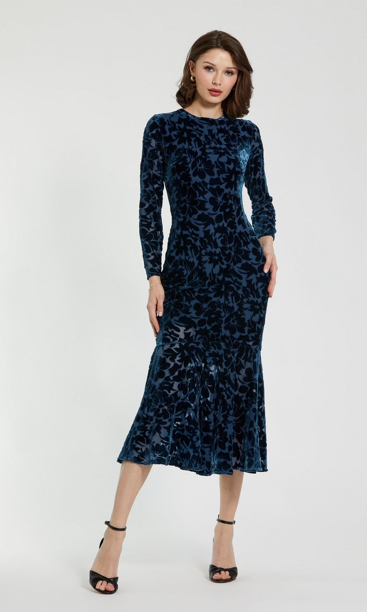 A woman stands wearing the Midi Party Dress: Mac Duggal 81129—a deep blue, long-sleeved burnout velvet midi dress with a floral pattern—paired with black high-heeled sandals against a plain light background. Ideal as a party dress, this look captures effortless elegance.